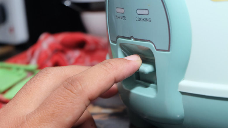 Une main appuie sur le bouton de cuisson d'un cuiseur à riz bleu sarcelle