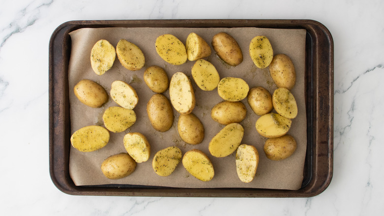 Pommes de terre crues assaisonnées sur une plaque à pâtisserie