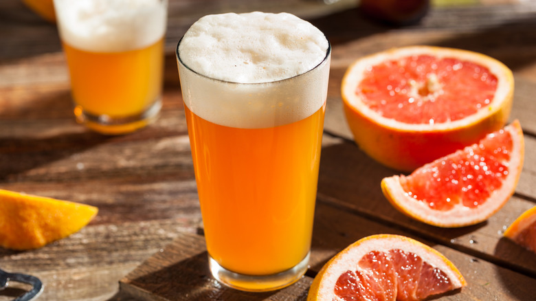 Une bière mousseuse sur une table en bois avec des moitiés et des quartiers de pamplemousse disposés dans le cadre.