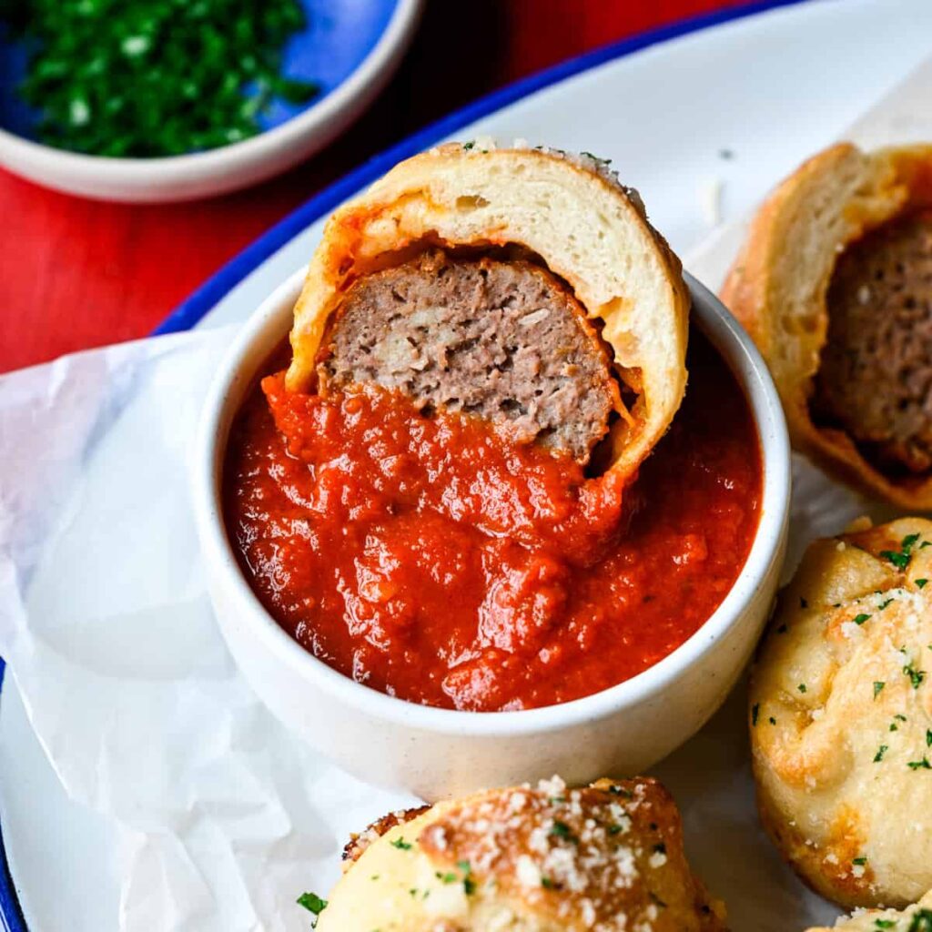 Close up view of a halved meatball sub bite dipped into a bowl of marinara.