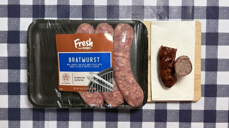 Paquet de bratwurst Meijer à côté de brat cuit coupé en deux sur une nappe à carreaux