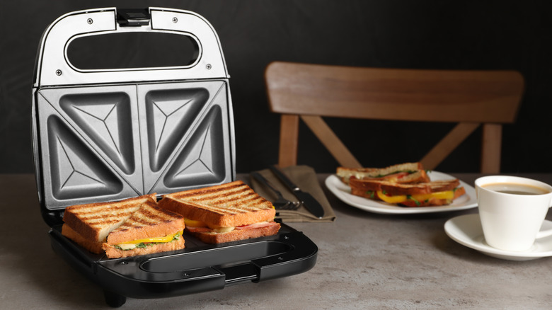 toastie grill maker avec de délicieux sandwichs et une tasse de café sur une table gris clair