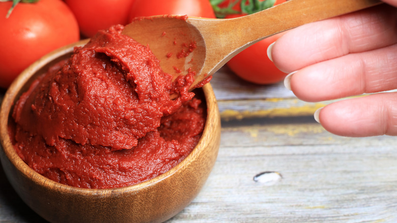 Une main ramassant de la pâte de tomate avec une cuillère en bois