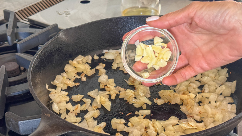 main ajoutant l'ail à la poêle avec les oignons