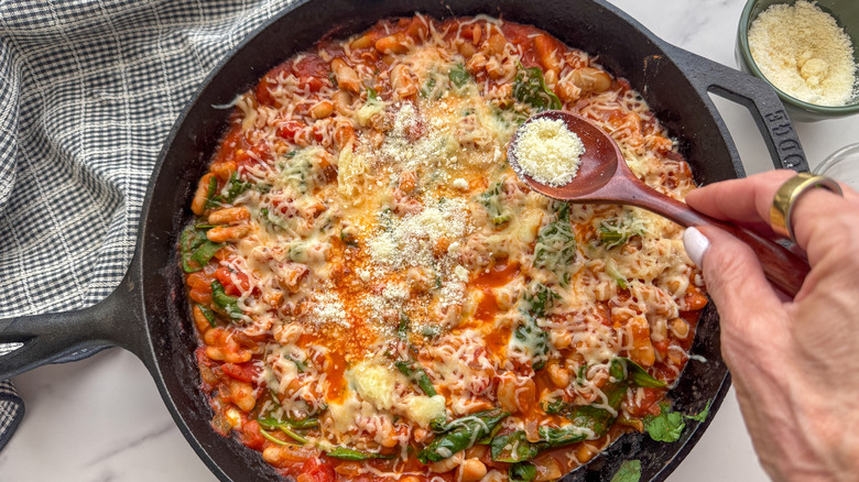 Saupoudrer à la main du parmesan sur une poêle à haricots