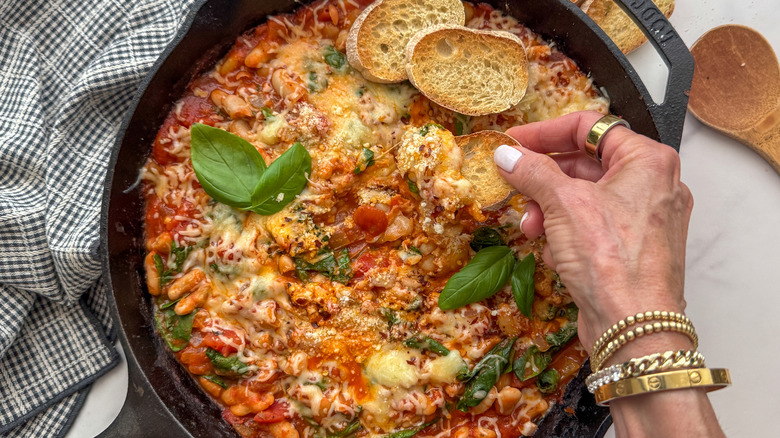 Tremper à la main une tranche de baguette dans une poêle à grains de pizza