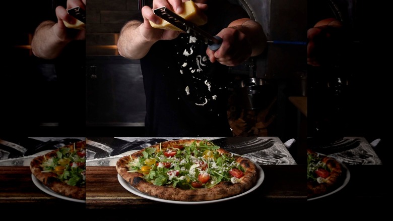 On voit les mains d'une personne en train de raser du parmesan sur une pizza chez Razza Pizza Artigianale à Jersey City, New Jersey