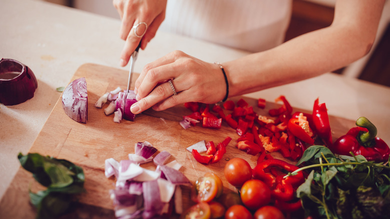 Personne coupant des oignons, des poivrons rouges et des tomates