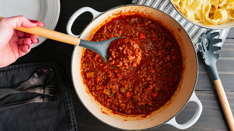 Personne préparant la sauce bolognaise au four hollandais, un bol de pâtes visible en arrière-plan