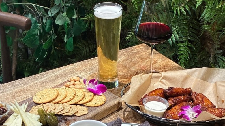 Une planche de charcuterie à gauche, de la bière et du vin au milieu et des ailes de poulet à droite, le tout servi sur une table.