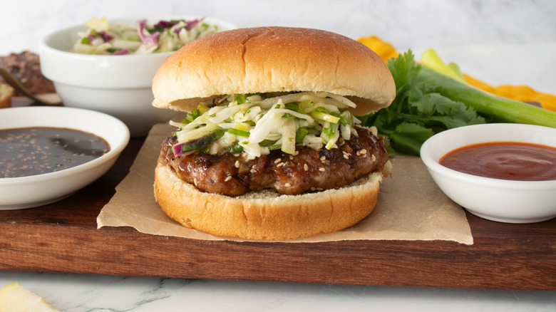 Un plan latéral d'un hamburger assemblé garni de salade de chou entouré de condiments et de garnitures