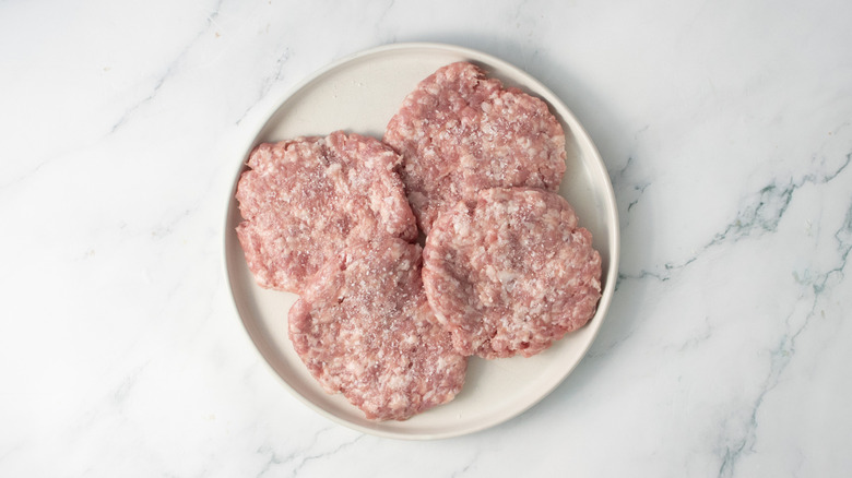 Galettes de porc crues assaisonnées de sel sur une assiette blanche