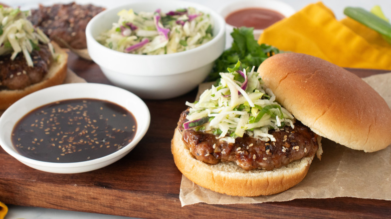Un plan latéral d'un hamburger assemblé garni de salade de chou entouré de condiments et de garnitures