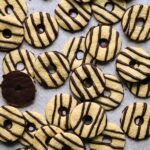 Overlapping homemade fudge stripe cookies scattered on parchment paper, with one cookie flipped over to show its chocolate-coated bottom.