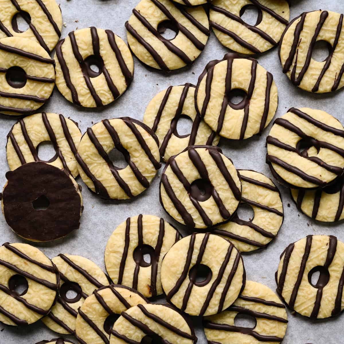 Biscuits à rayures au fudge faits maison qui se chevauchent, éparpillés sur du papier parchemin, avec un biscuit retourné pour montrer son fond enrobé de chocolat.