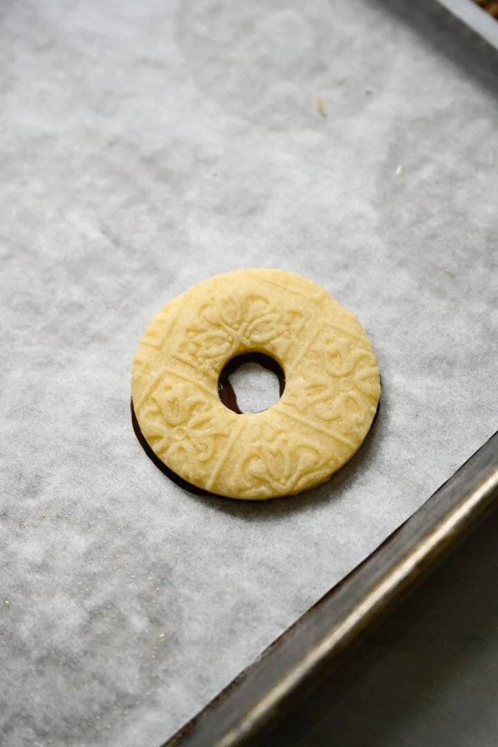Biscuit sablé en forme d'anneau en relief pressé sur un anneau de chocolat fondu sur une plaque à pâtisserie tapissée de papier sulfurisé.