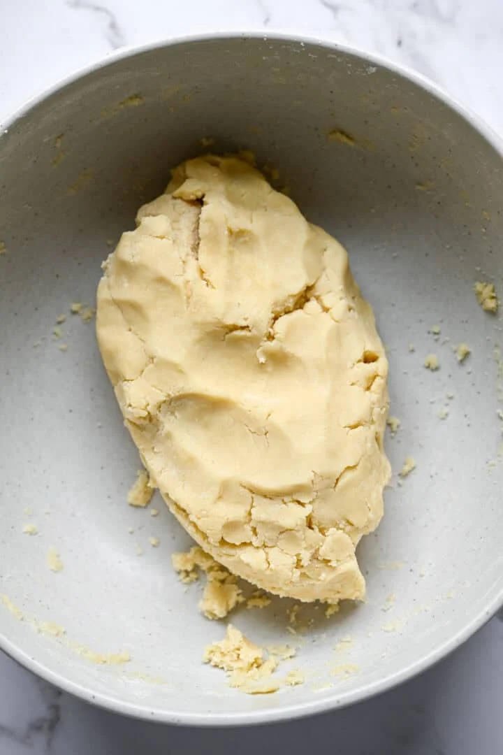Lisser un tas de pâte à biscuits sablés dans un grand bol à mélanger moucheté avec quelques miettes autour.