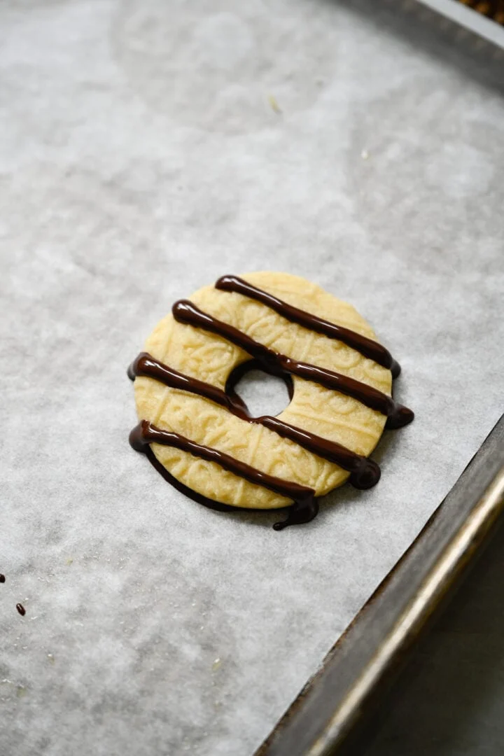 Biscuit sablé unique en forme d'anneau avec un fond enrobé de chocolat et quatre bandes de chocolat noir arrosées sur le dessus.