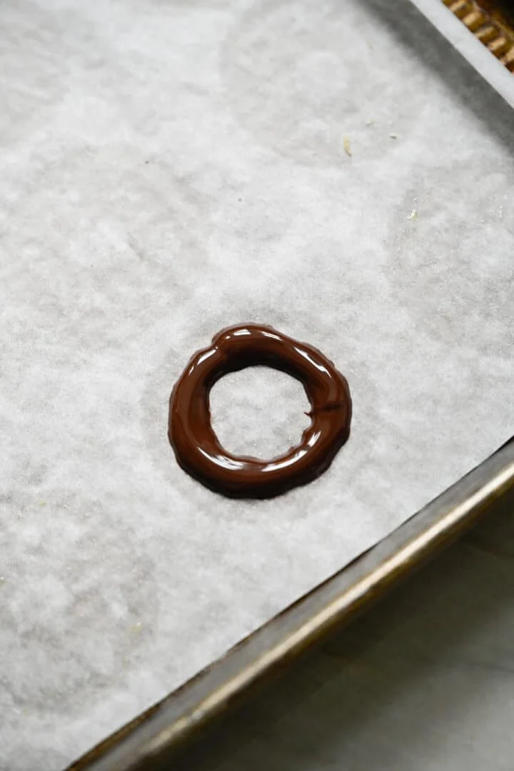 Anneau de chocolat noir fondu déposé sur une plaque à pâtisserie tapissée de papier sulfurisé.