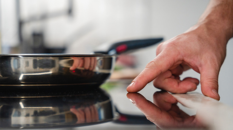 Une main appuyant sur un capteur sur une table de cuisson à induction avec une casserole posée sur le brûleur