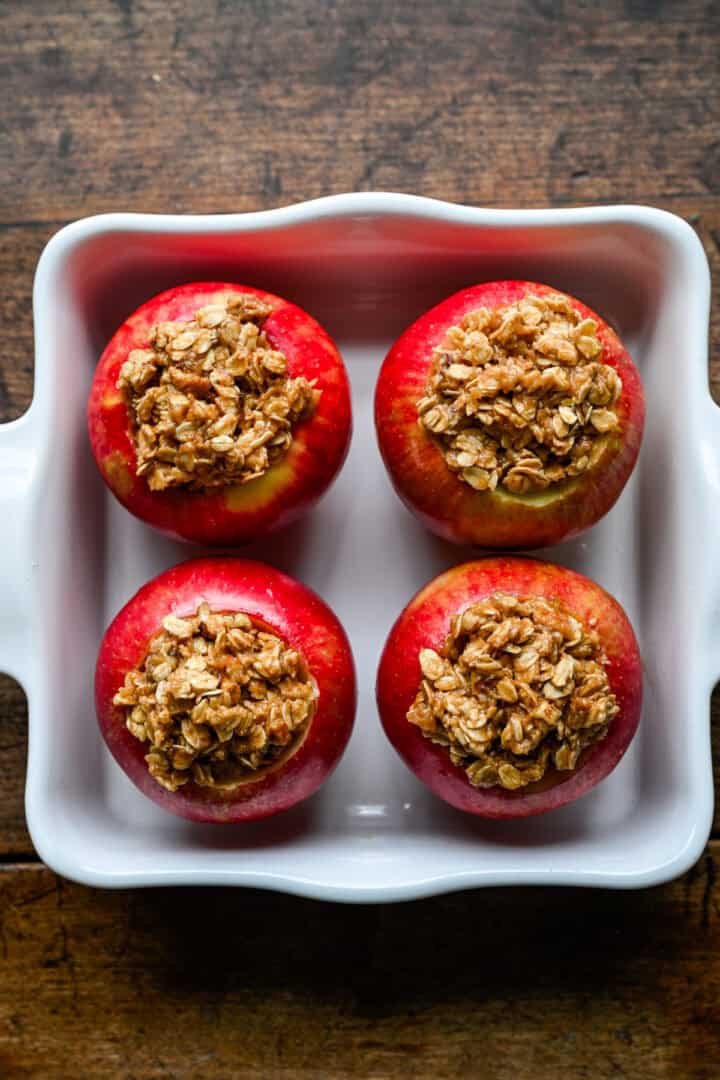 Pommes évidées remplies de crumble d'avoine dans un plat allant au four blanc avant la cuisson.