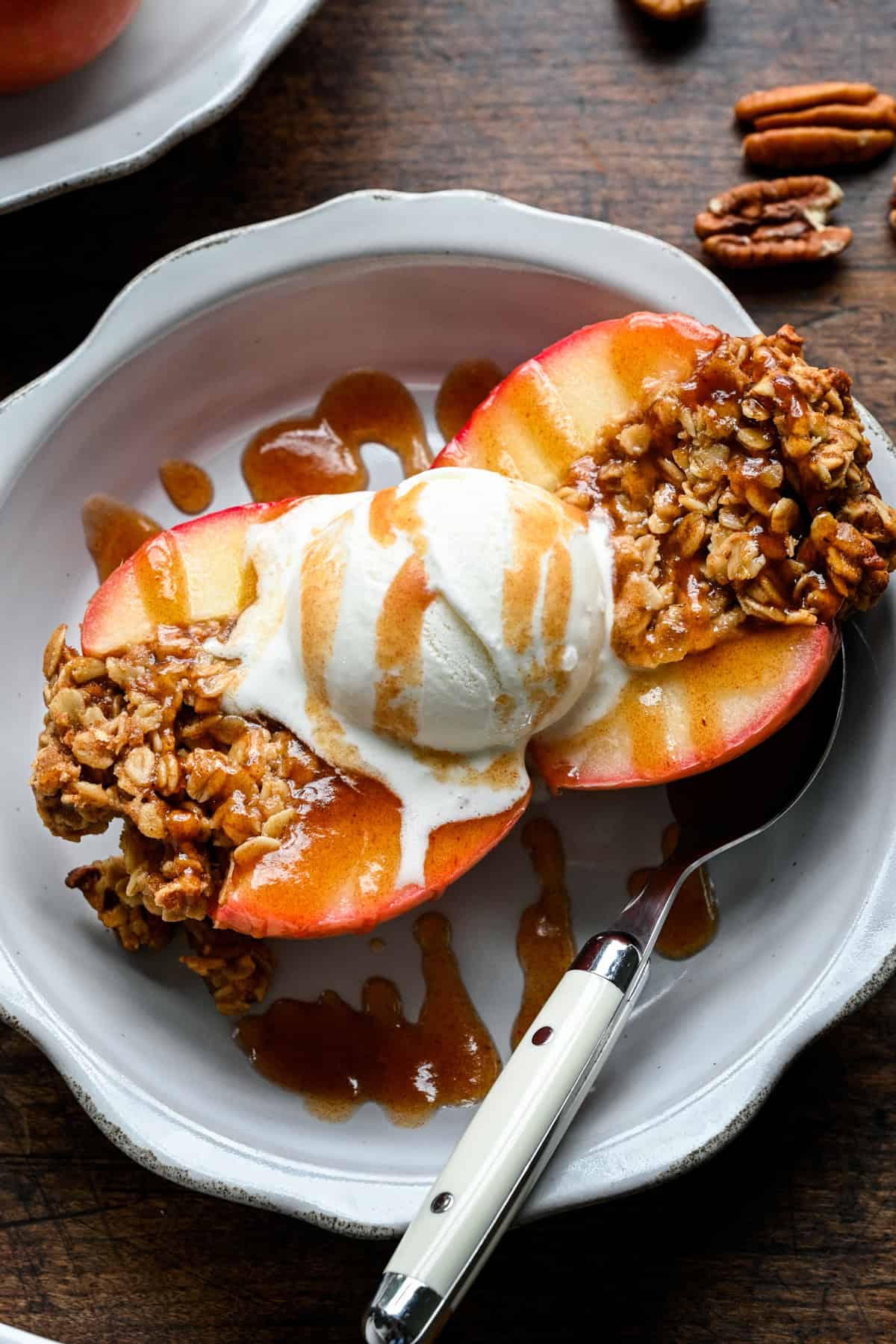Vue rapprochée d'une pomme cuite ouverte, glace à la vanille fondant dans le crumble d'avoine avec une accumulation de caramel aux dattes sur l'assiette.