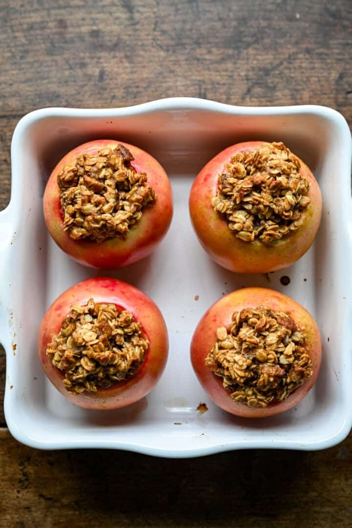 Les mêmes quatre pommes après cuisson, la peau ramollie et ridée et la garniture d'avoine dorée.