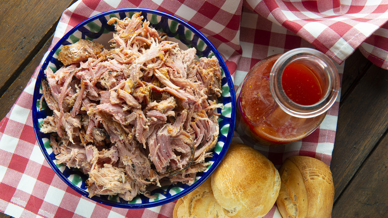 Un bol de porc effiloché avec une bouteille de sauce barbecue et des petits pains