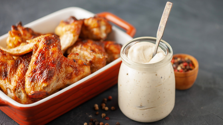 Un pot de sauce barbecue blanche Alabama à côté d'un plat de poulet barbecue