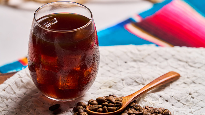 Un verre d'infusion froide avec de la glace et une cuillère en bois avec des grains de café