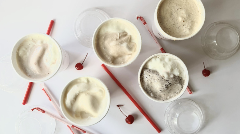 Milkshakes Chick-fil-A à moitié consommés sur une surface blanche avec des cerises, des pailles et des couvercles