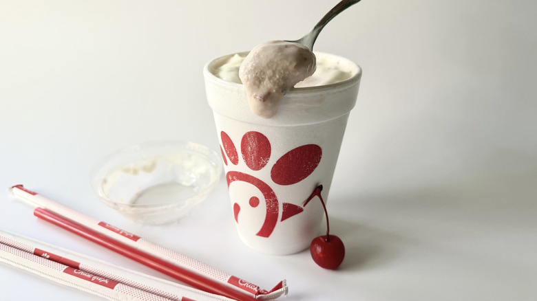 Milkshake aux fraises de Chick-fil-A avec une cuillère insérée dans la tasse à côté d'une cerise, des pailles et du couvercle
