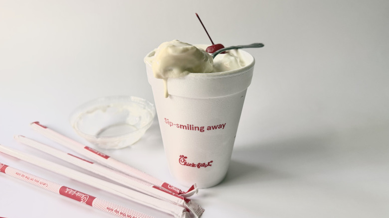 Milkshake à la vanille de Chick-fil-A avec une cuillère sur la tasse à côté d'une cerise, des pailles et du couvercle
