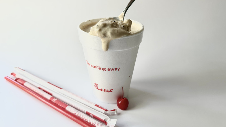 Milkshake S'mores de Chick-fil-A avec une cuillère insérée dans la tasse à côté d'une cerise, des pailles et du couvercle