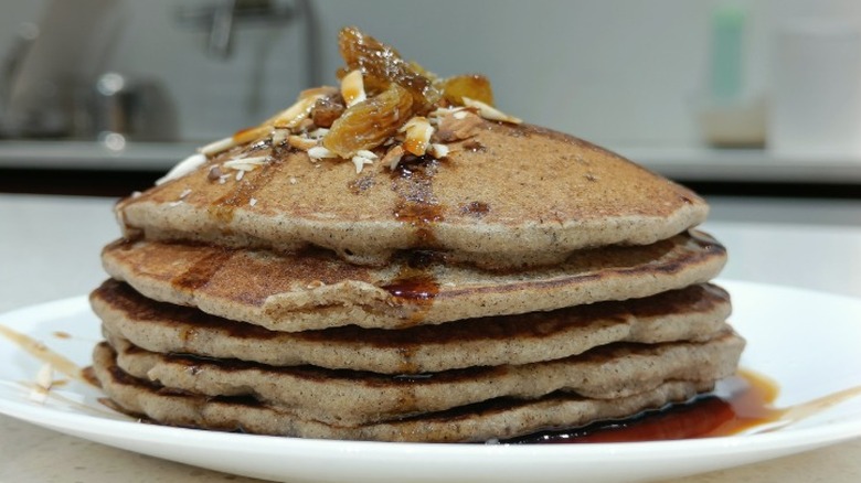 Une pile de gâteaux de sarrasin sur une assiette avec du sirop partout dessus.
