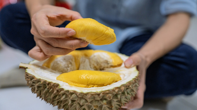 Les mains d'une personne présentant un fruit durian ouvert