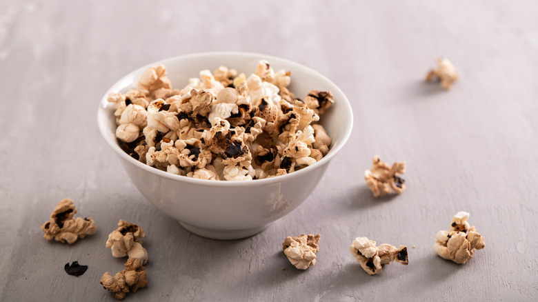 Pop-corn partiellement brûlé dans un bol blanc, avec des morceaux de pop-corn à l'extérieur