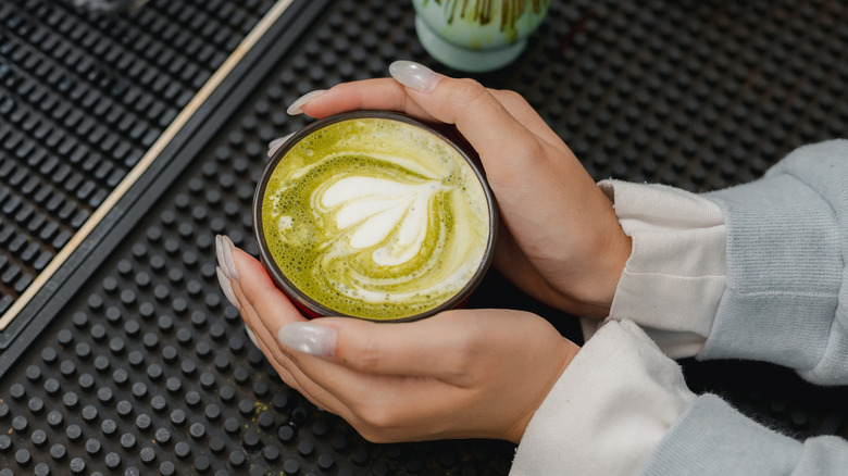 On voit les mains d’une personne en train de prendre un matcha latte.