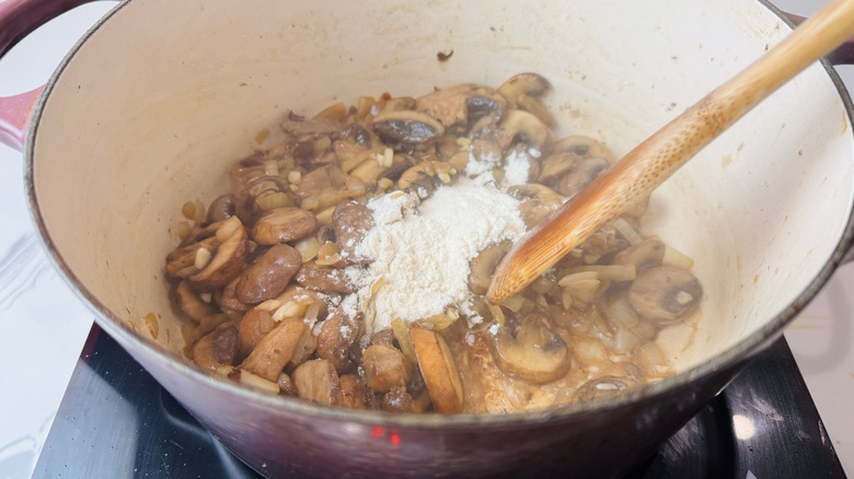 Champignons, farine et cuillère en bois dans une cocotte