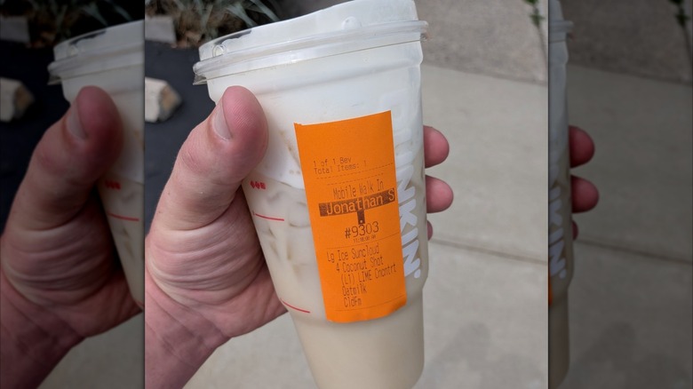 Personne tenant du citron vert à la noix de coco dans une grande tasse Dunkin' en plastique