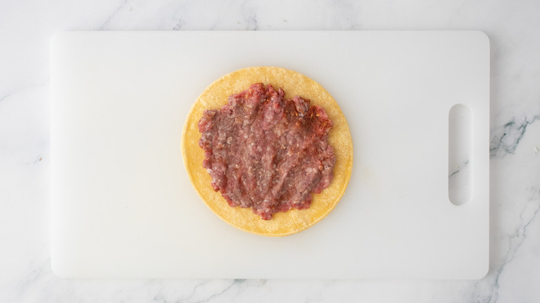 Une tortilla de maïs avec une galette de burger écrasée dessus