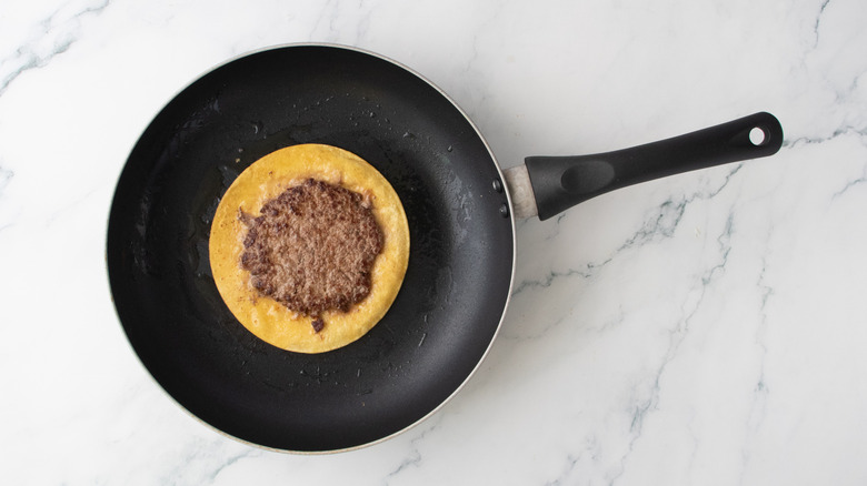 Une galette de burger poêlée sur une tortilla de maïs dans une poêle antiadhésive
