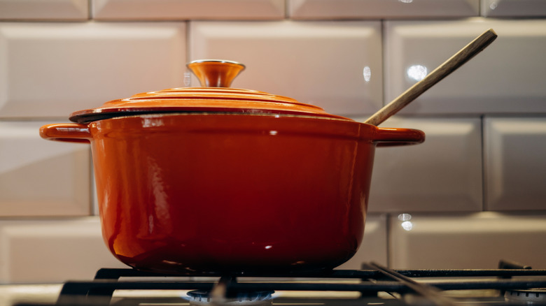 Four hollandais en fonte sur une cuisinière avec une cuillère en bois qui sort du dessus