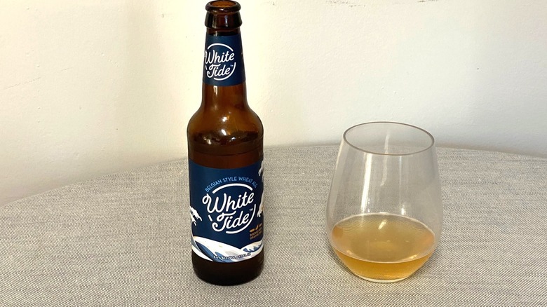 Une bouteille de bière White Tide sur une table à côté d'un échantillon dans un verre