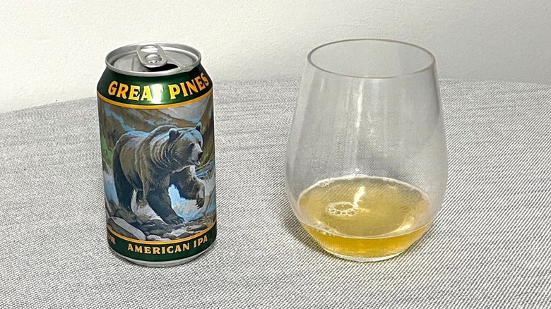 Une canette de Great Pines American IPA sur une table à côté d'un échantillon dans un verre