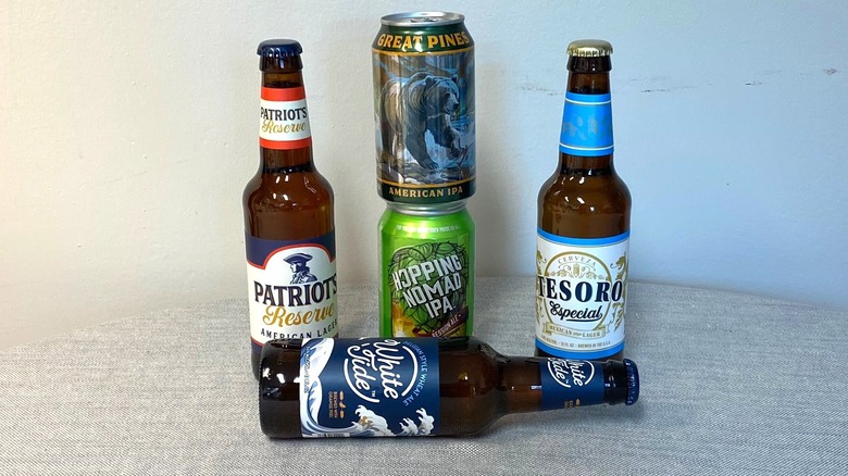 Cinq bières Aldi disposées sur une table, avec deux canettes empilées et une bouteille posée