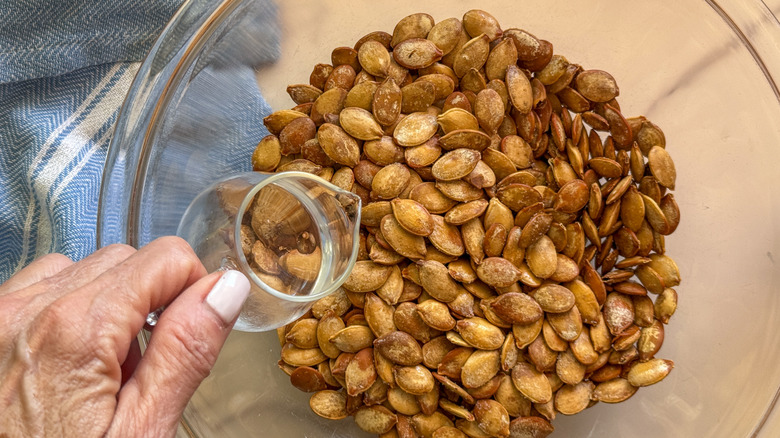 Verser à la main du vinaigre sur des graines de citrouille grillées dans un bol