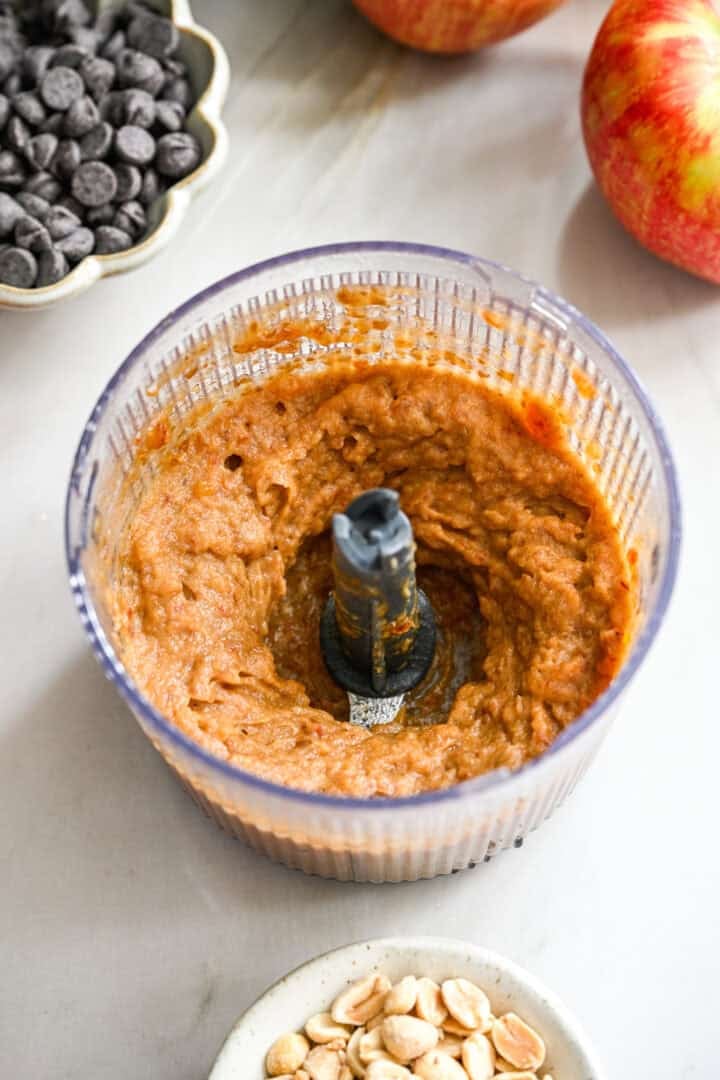 Vue à 45 degrés des dattes mélangées en une pâte épaisse dans un petit robot culinaire.