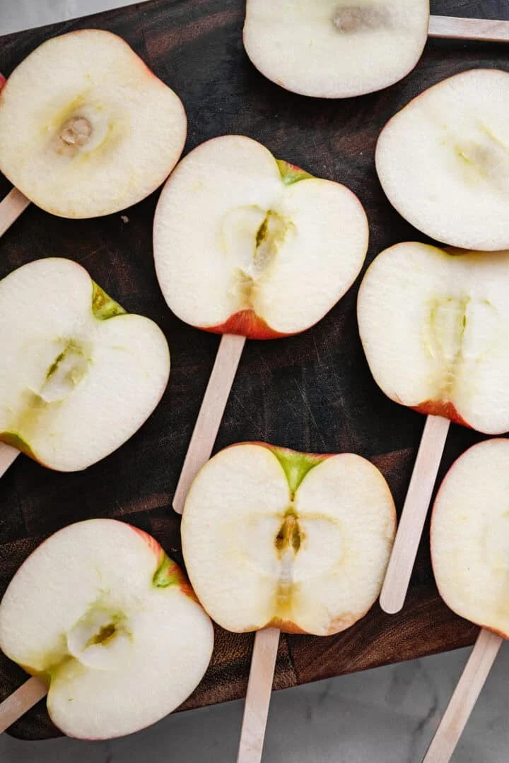 Vue aérienne de tranches de pomme épaisses sur des bâtons de glace sur une planche à découper en bois sombre.