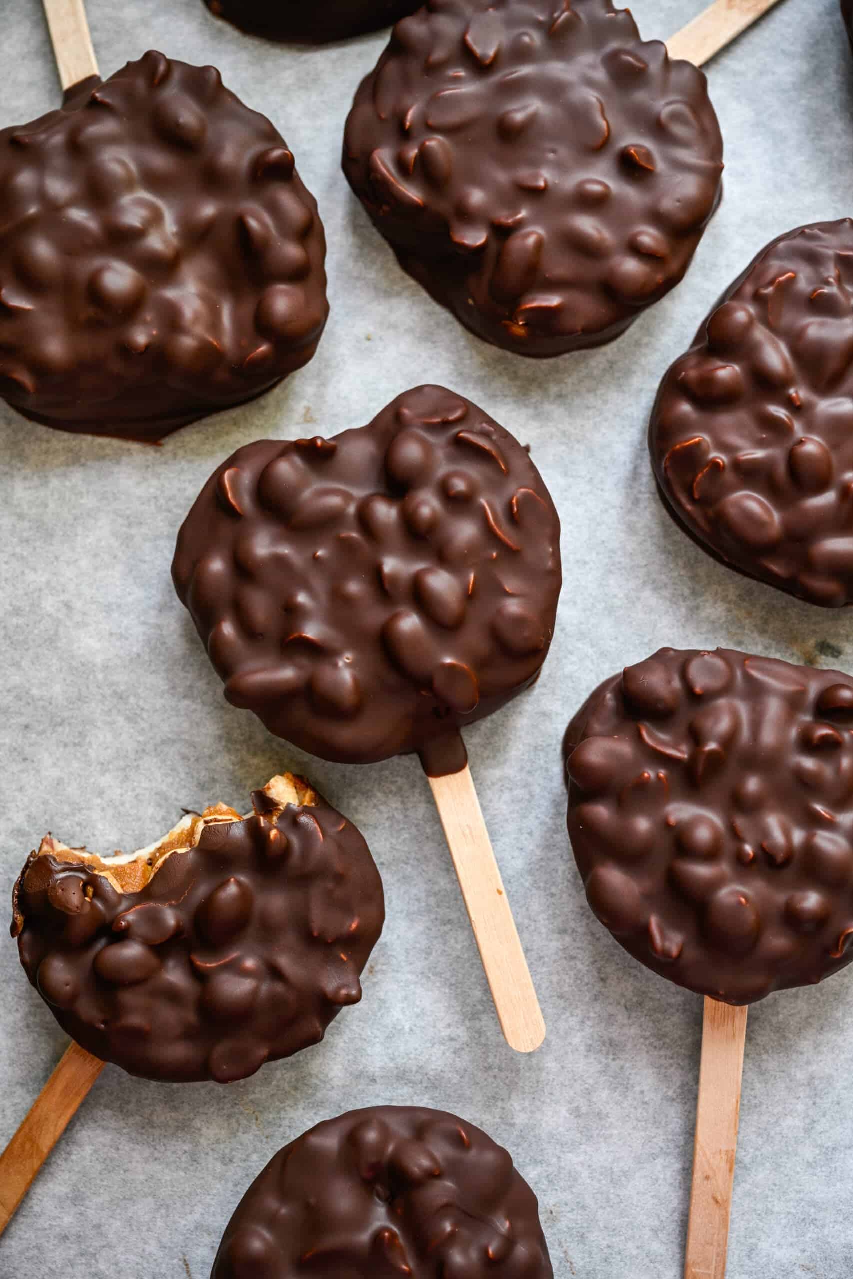 Vue aérienne de tranches de pomme enrobées de chocolat sur des bâtons de glace sur papier parchemin, dont une avec une bouchée retirée.